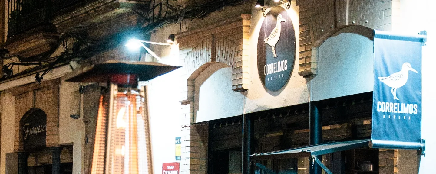 La fachada de noche, con el cartel del correlimos y la terraza llena
